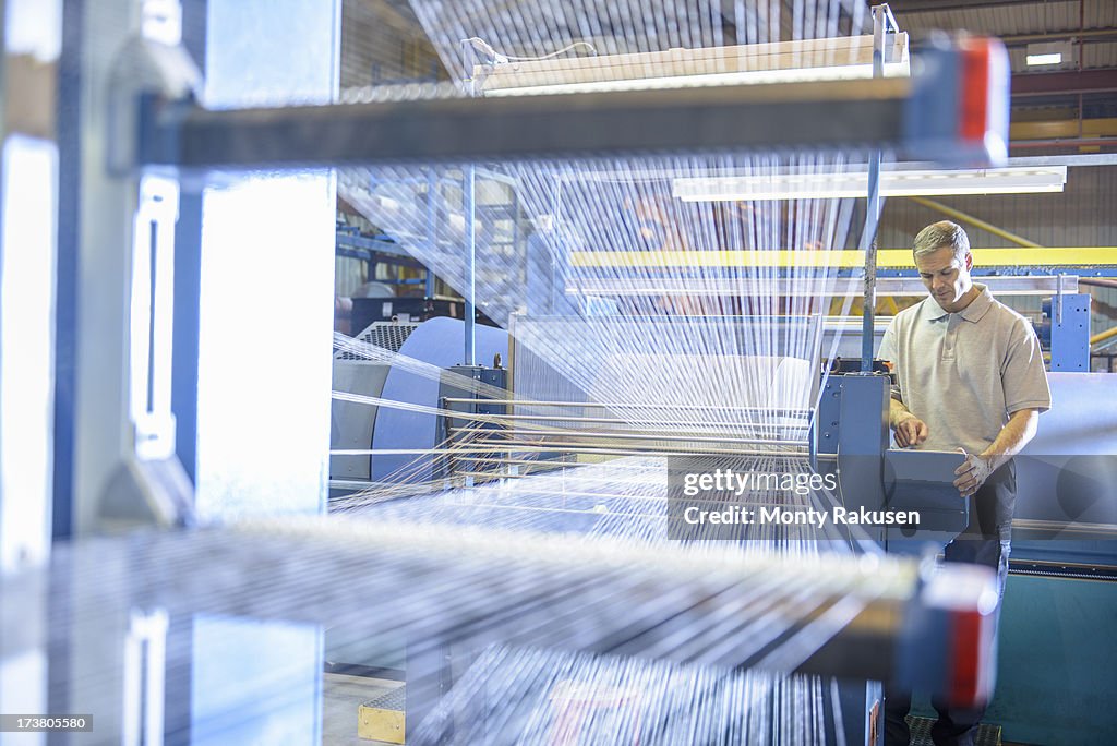 Textile worker inspecting threads on loom in mill