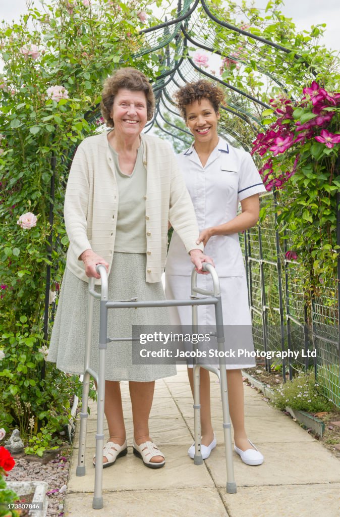 Caretaker helping older woman use walker