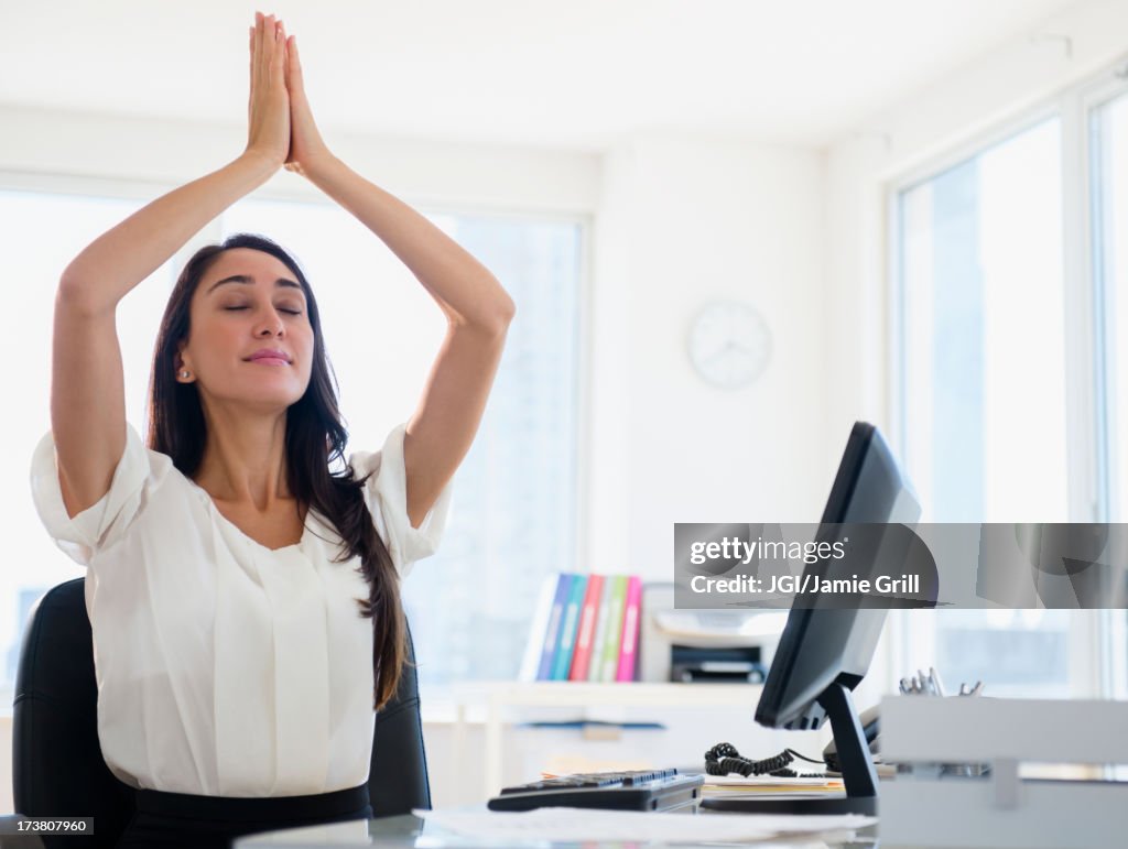 Caucasian businesswoman meditating at desk