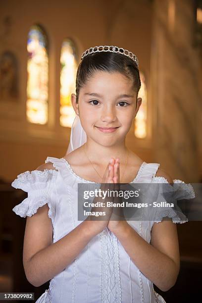 hispanic girl with hands clasped in church - prima comunione foto e immagini stock