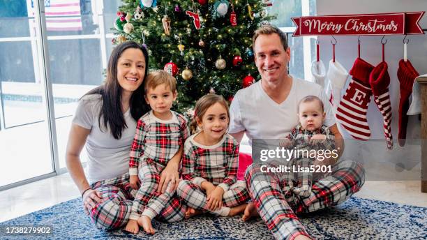 cute happy multiracial family in matching family pajamas under the christmas tree, mother and father with three young children - matching christmas pajamas stock pictures, royalty-free photos & images