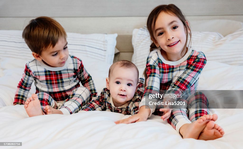 Three cute kids at home in bed wearing matching Christmas pajamas