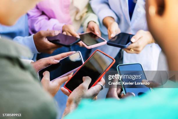 young group of people standing in circle using mobile phones outside. unrecognizable teen friends watching social media content on smartphone app. technology lifestyle concept. - social networking foto e immagini stock