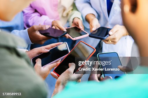 Young group of people standing in circle using mobile phones outside. Unrecognizable teen friends watching social media content on smartphone app. Technology lifestyle concept. Young group of people standing in circle using mobile phones outside. Unrecognizable teen friends watching social media content on smartphone app. Technology lifestyle concept.