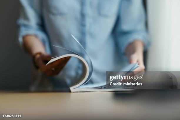 an unrecognizable woman turning pages of a book in a library - publication stock pictures, royalty-free photos & images