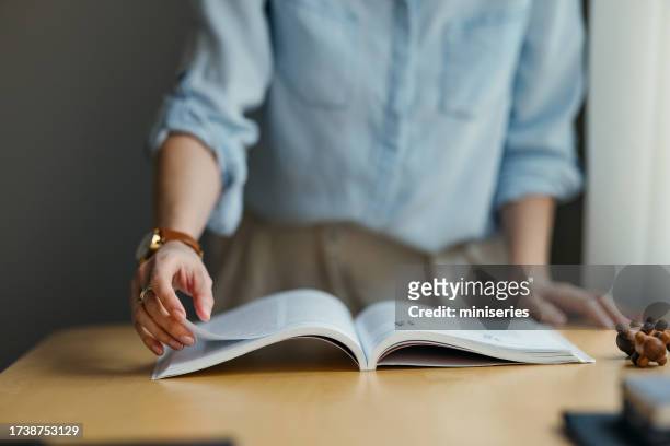 una donna irriconoscibile che gira le pagine di un libro in una biblioteca - sfogliare libro foto e immagini stock