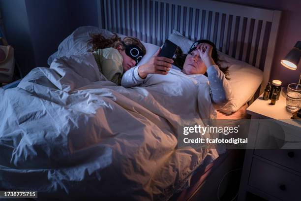 mother checking mobile phone while daughter is sleeping beside her - bedside table kid asleep stock pictures, royalty-free photos & images