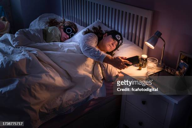 mother looking at mobile phone while daughter is sleeping beside her - bedside table kid asleep stock pictures, royalty-free photos & images