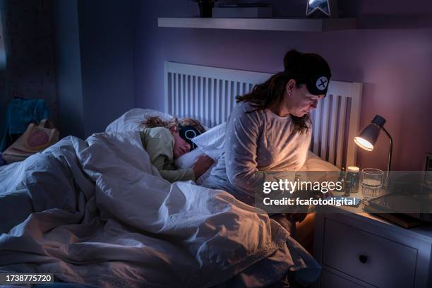 mother checking mobile phone while daughter is sleeping beside her - bedside table kid asleep stock pictures, royalty-free photos & images