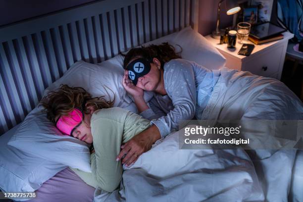 mother and daughter wearing eye masks sleeping together - bedside table kid asleep stock pictures, royalty-free photos & images
