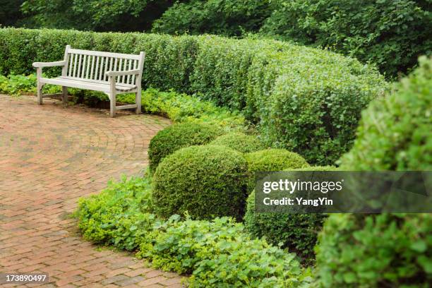 brick garden patio and wood bench in lush planted landscape - vormsnoeikunst stockfoto's en -beelden
