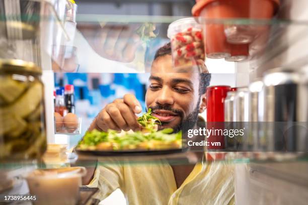 delighted young black man looking at food in his refrigerator - beverage fridge stock pictures, royalty-free photos & images