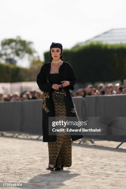 Guest wears a scarf over the head, a choker, low neck top, a long jacket with a printed / embroidered drawing, leather bag, brown and beige zebra...