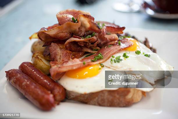 a closeup of eggs, bacon, ham, and sausage on top of toast - american culture stockfoto's en -beelden