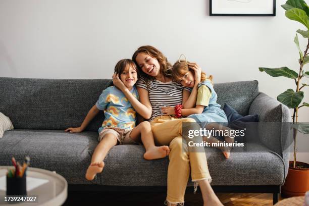 a happy beautiful woman keeping her eyes closed while enjoying spending her leisure time at home with her cute children - family happy living room stock pictures, royalty-free photos & images