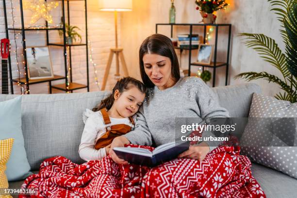 mother reading a storybook to her daughter on christmas - curled up reading book stock pictures, royalty-free photos & images