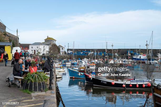 People sit on the quayside by the Inner Harbour and fishing boats on September 17, 2023 in Mevagissey, England.