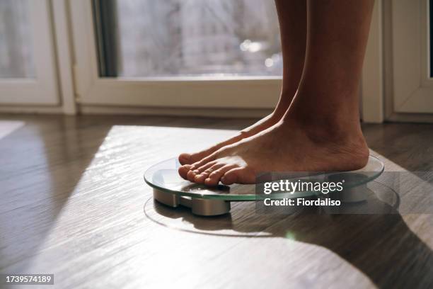 a middle-aged woman standing in the morning on the scales - anorexie stock pictures, royalty-free photos & images