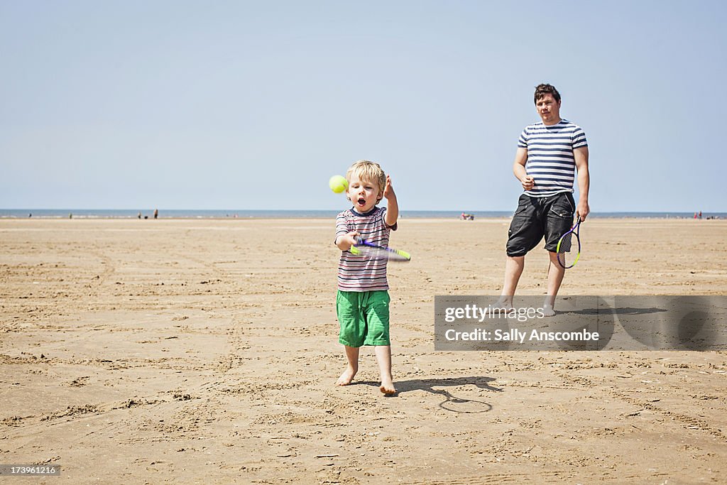 Father and son playing tennis on the beach
