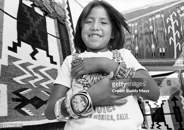 Young Navajo girl shows off jewelry made by her mother, a Navajo Silversmith, at an art fair in Pecos, New Mexico, 1977. .