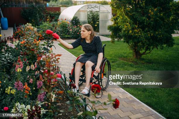 girl with cerebral palsy in a wheelchair enjoys the beauty of nature in her garden - world kindness day stock pictures, royalty-free photos & images
