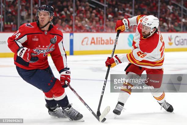Dillon Dube of the Calgary Flames shoots into John Carlson of the Washington Capitals during the first period at Capital One Arena on October 16,...