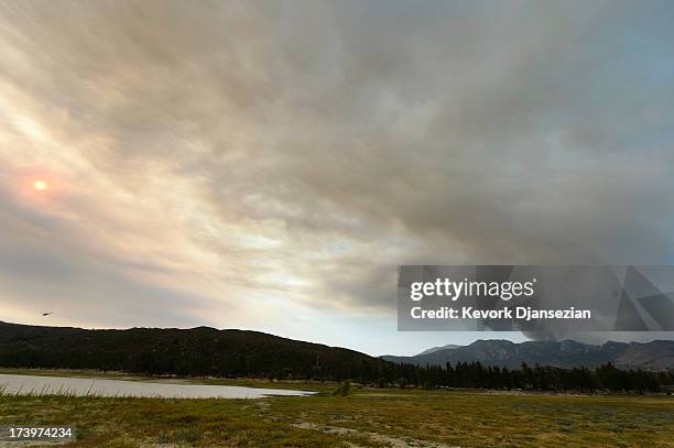 Fire fighting helicopter heads to Lake Hemet to pick up water as a larg plum of smoke rises to the sky from the out to control Mountian Fire on July...