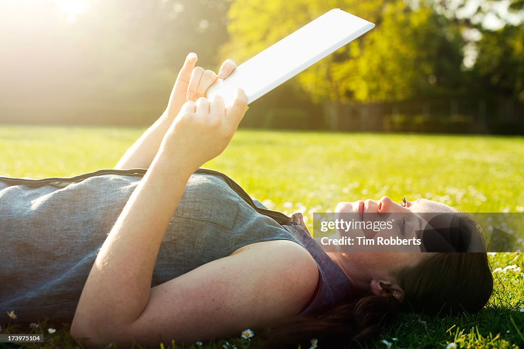 Young woman lying on grass with digital tablet.