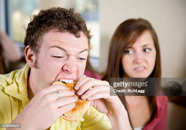junger mann essen einen cheeseburger - angry rich guy stock-fotos und bilder