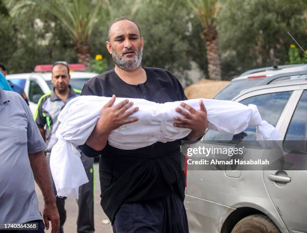 Palestinian man carries the body of a child killed during Israeli air raids on October 17, 2023 in Khan Yunis, Gaza. Gazans are evacuating to the...