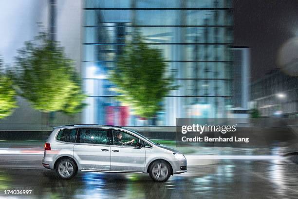 car driving down urban street in rain - street side stock-fotos und bilder