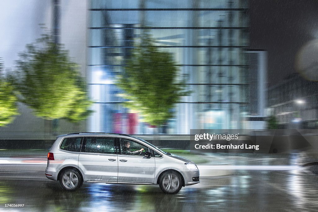 Car driving down urban street in rain