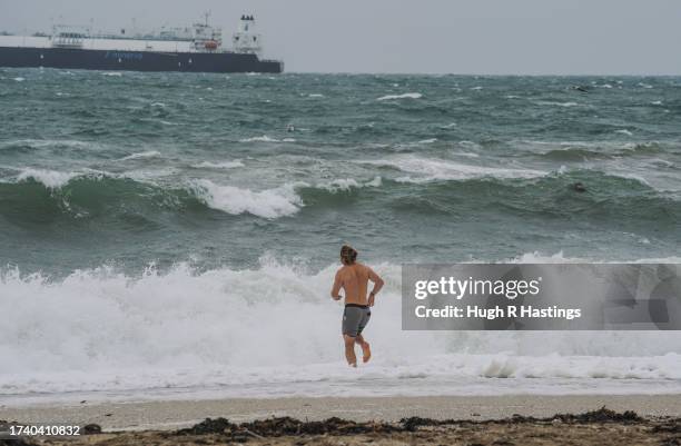 Member of the public makes their way into the sea for a morning swim in rough seas at Gyllyngvase Beach as strong winds arrive on the coastline on...