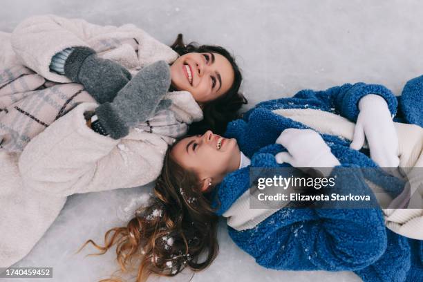 two female friends in warm fur coats and scarves are having fun skating on ice and laughing in a winter park outdoors. happy smiling teens girls in warm clothes walk together during the winter holidays in december - cute girlfriends stock-fotos und bilder