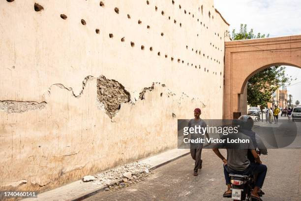 Deux hommes sur un scooter observent un mur endommagé suite au séisme dans la Médina de Marrakech le 14 septembre 2023.