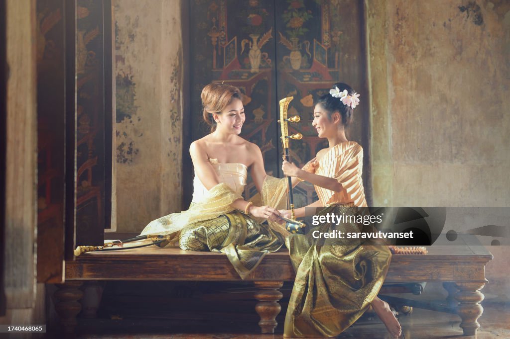 Two Asian women in traditional Thai clothing with a Thai Saw Duang stringed instrument, Thailand
