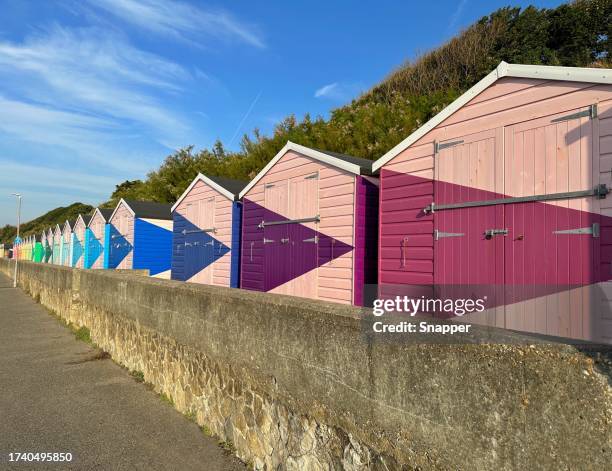 row of multi coloured wooden beach huts on beach, folkestone, kent, england, uk - folkestone stock pictures, royalty-free photos & images