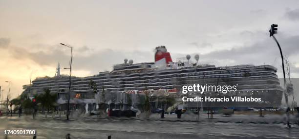 Queen Victoria, a 90,049 GT Vista-class cruise ship operated by the Cunard Line, is seen through an automobile windshield during heavy rain while...