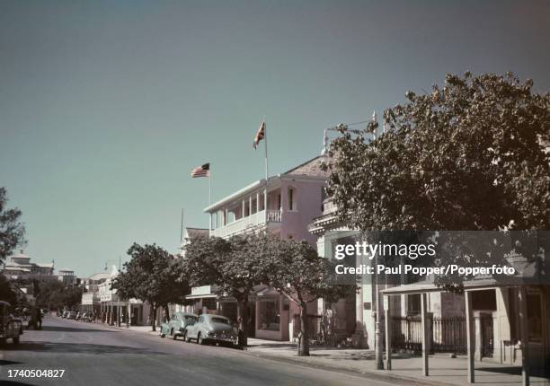 Pedestrians pass cars parked in front of the Prince George Hotel on Bay Street in Nassau, The Bahamas, circa 1950.