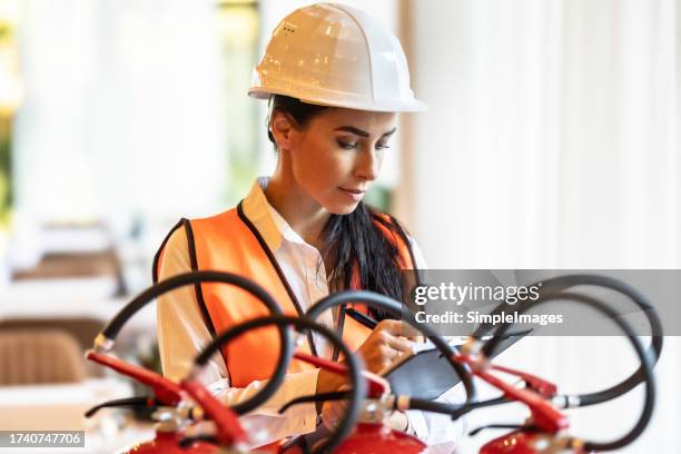 a female safety inspector checks the fire extinguishers in the hotel restaurant. - fire extinguisher inspection stock pictures, royalty-free photos & images