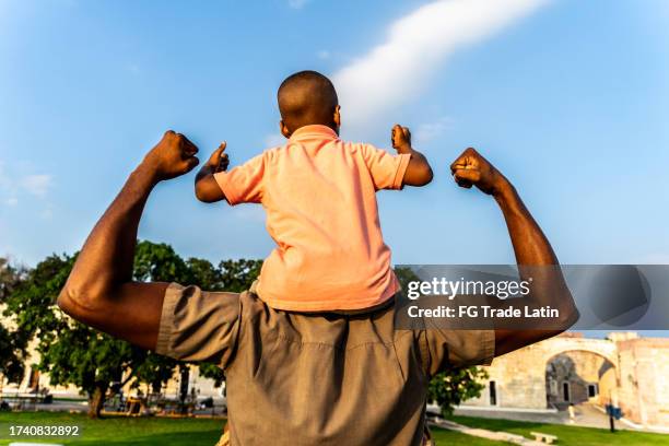 vista posteriore di un padre con suo figlio che flette i muscoli all'aperto - mascolinità foto e immagini stock