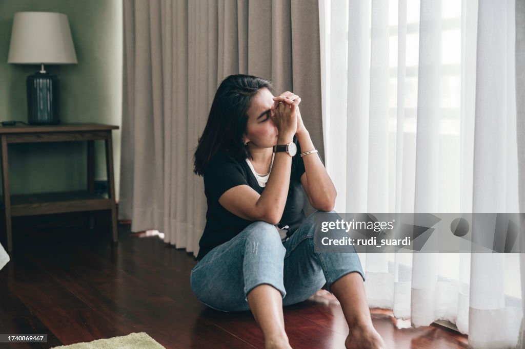 Sad and depressed woman sitting alone at home on the floor