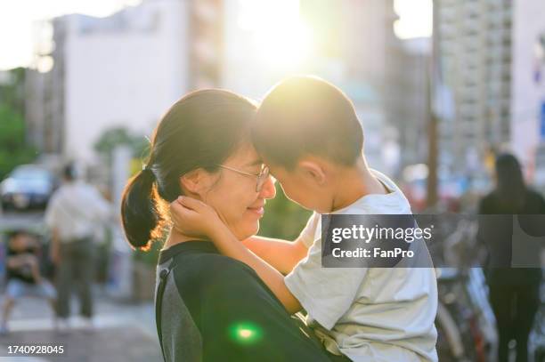 a loving young asian mother lifting her little boy in the air against sunshine while spending time together in the city. enjoying mother and son moment. love and care. family, child and parenthood concept - east asia stock pictures, royalty-free photos & images