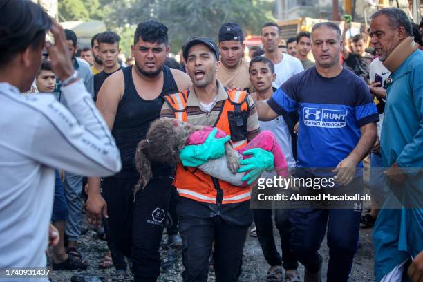 Palestinian emergency services and local citizens carry a young child as they search for victims in buildings destroyed during Israeli air raids in...
