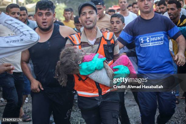 Palestinian emergency services and local citizens carry a young child as they search for victims in buildings destroyed during Israeli air raids in...