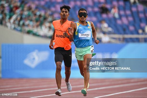 India's Ankur Dhama accompanied by his guide crosses the finish line to win the men's 5000m-T11 final at the Huanglong Sport Centre Stadium during...