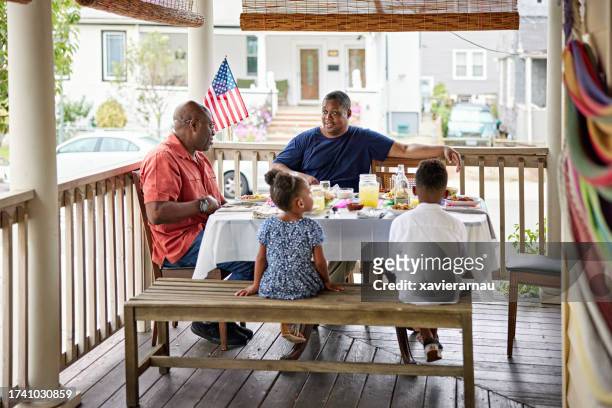 afroamerikanische männer und kinder sitzen zum mittagessen im freien - familie zuhause essen stock-fotos und bilder