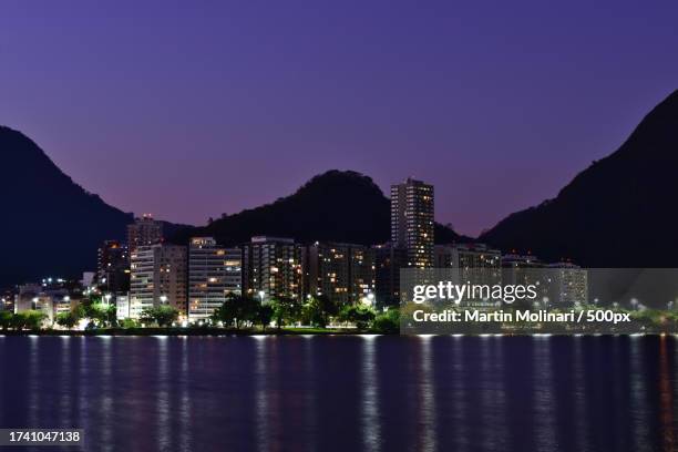 scenic view of illuminated buildings by sea against sky at night - molinari stock pictures, royalty-free photos & images