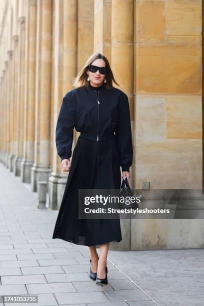 Influencer Annette Weber, wearing a black skirt by Max Mara, a black blouson by COS, a black bag by COS, black pumps by Valentino and sunglasses by...