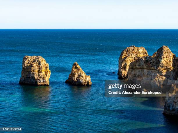 blue water and yellow huge rocks on the ocean shore. portugal. - klippe fotografías e imágenes de stock